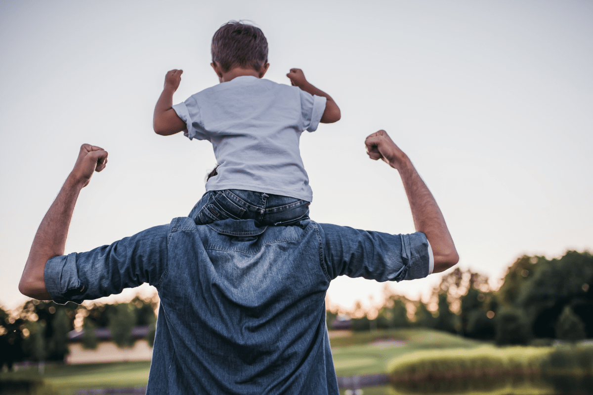 Boy on Mans shoulders, both are flexing their arms